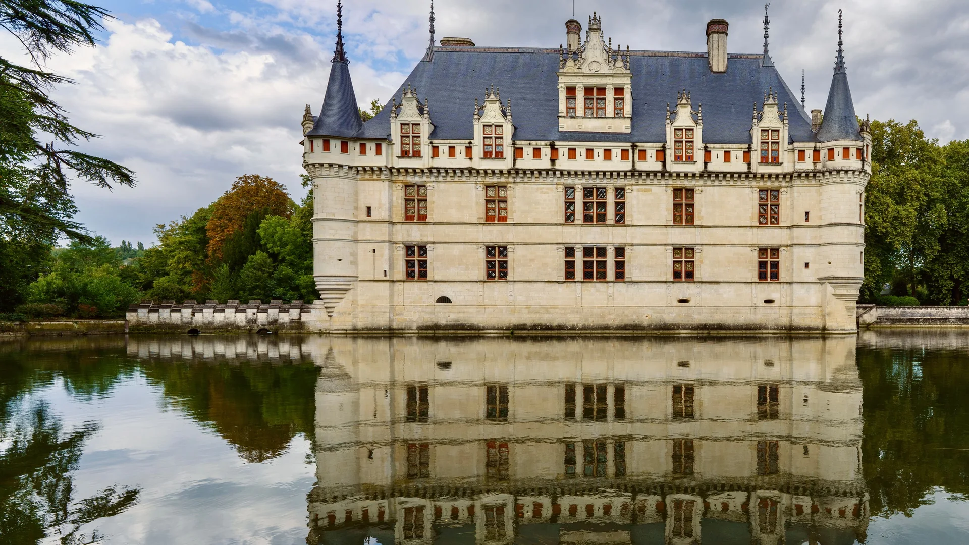 The pale stone façade, slate roofs and pointed turrets of the Château d'Azay-le-Rideau reflected whole in the still water of the Indre, framed by trees